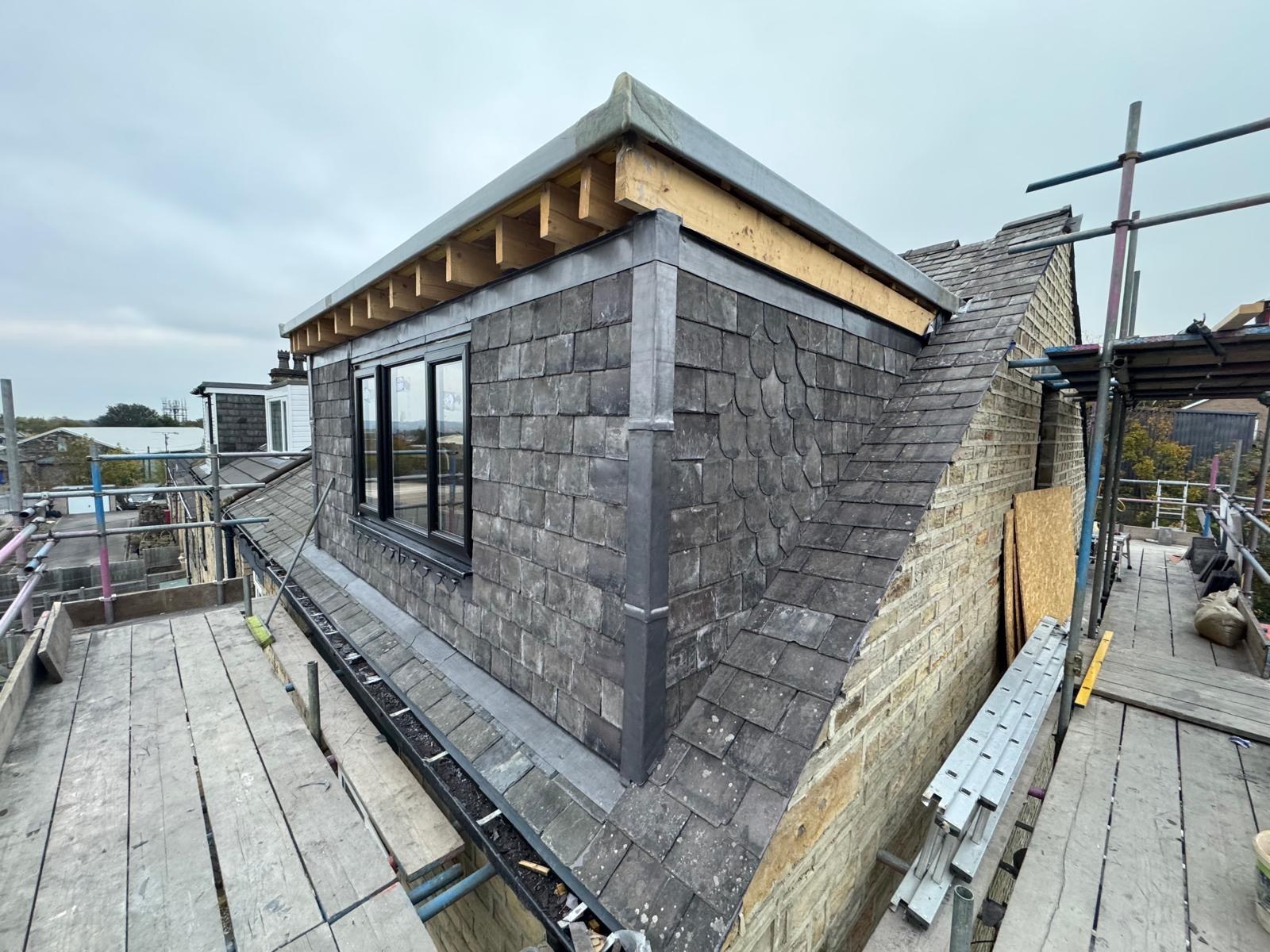Dormer windows, slate-clad cheeks and adjoining slate roof, photographed from the scaffold