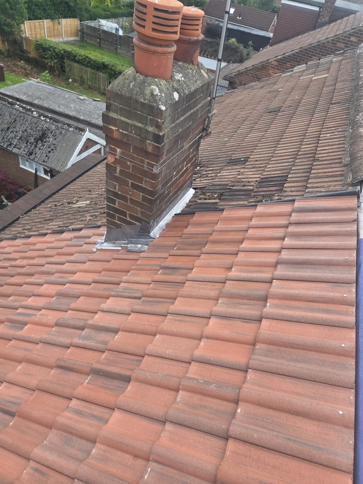 Brick chimney with terracotta pots and metal flashing at its base on a tiled roof
