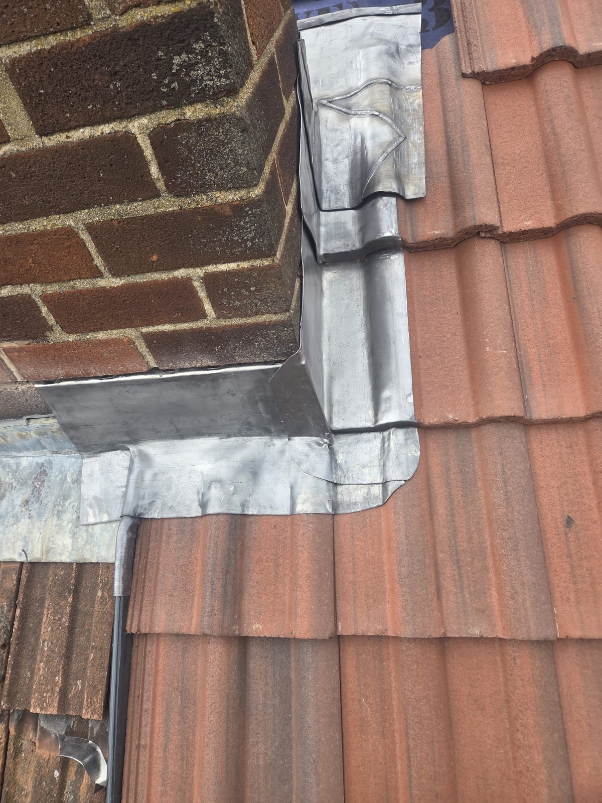 Close-up of metal flashing around the base of a brick chimney beside red roof tiles