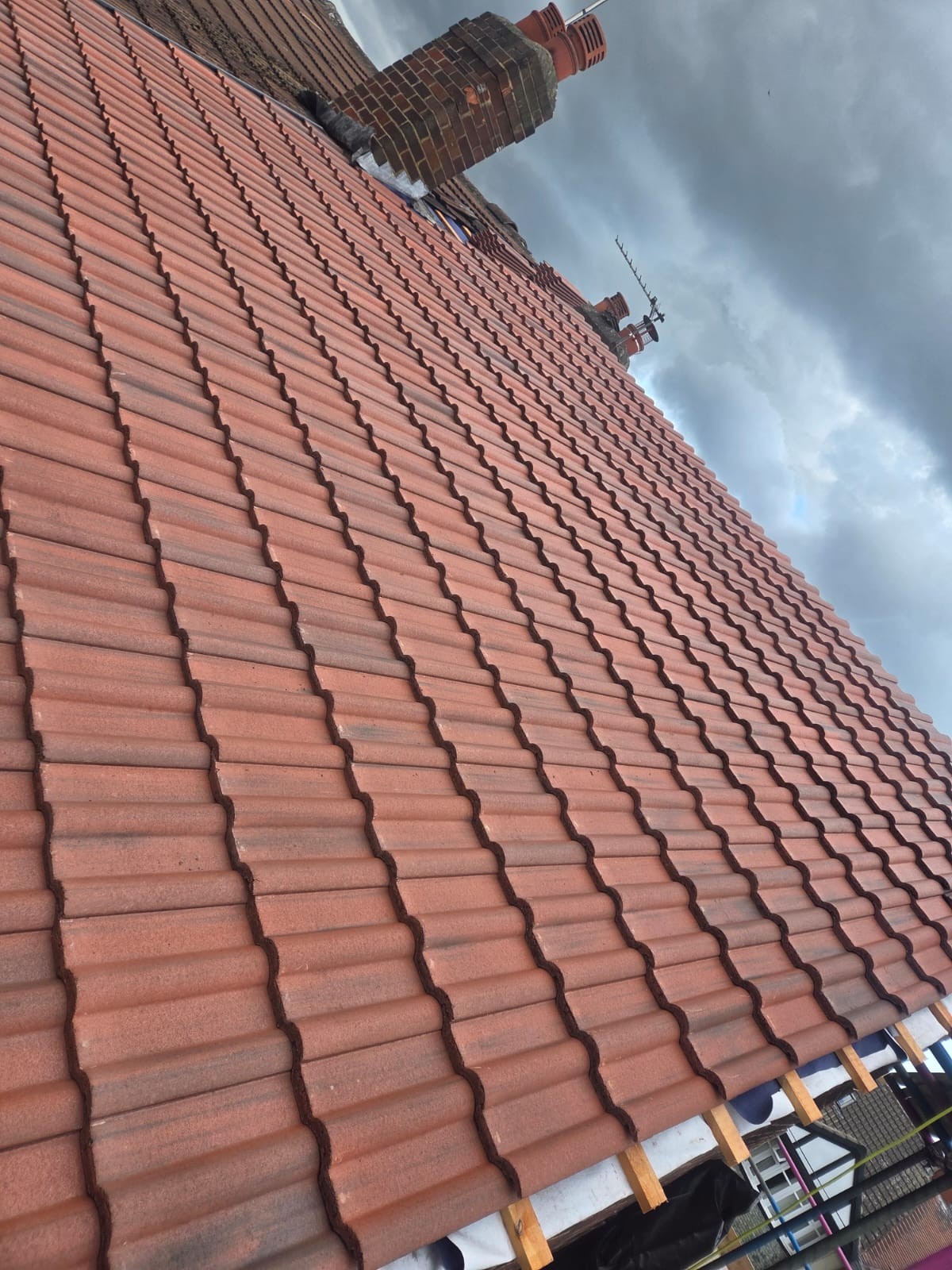 Rows of red roof tiles below a brick chimney, with scaffolding visible at the eaves