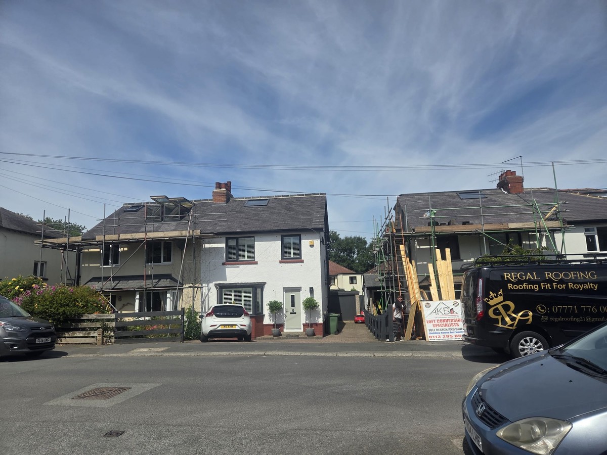 Two houses with scaffolding, roof coverings and exposed battens, beside a Regal Roofing van